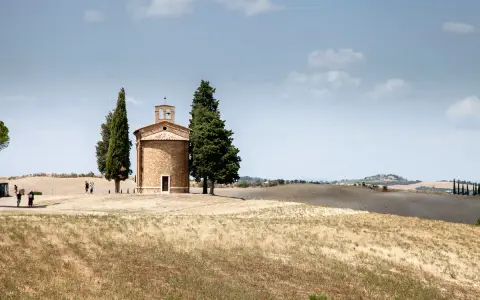 Cappella della Madonna di Vitaleta, icona della Val d'Orcia, circondata da cipressi e dolci colline toscane sotto un cielo azzurro.