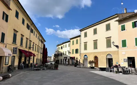 Piazza soleggiata a Pomarance, con edifici storici, tavolini all'aperto e scorci suggestivi da scoprire.