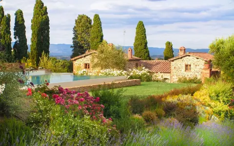 Vacanze in Toscana dove andare? Un casale in pietra con piscina, circondato da cipressi e un giardino fiorito.