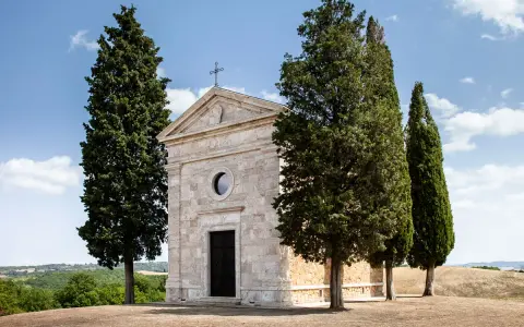 La chiesa di Vitaleta, con i suoi cipressi iconici, si erge solitaria su una collina toscana sotto un cielo azzurro.