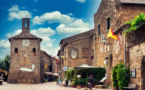 Un vicolo pittoresco a Sovana, Italia, con edifici in pietra, bandiere colorate e un cielo azzurro pieno di nuvole.