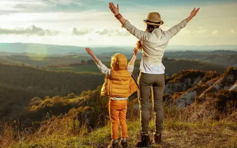 Bambini in Toscana, con le braccia al cielo, ammirano un paesaggio collinare al tramonto.