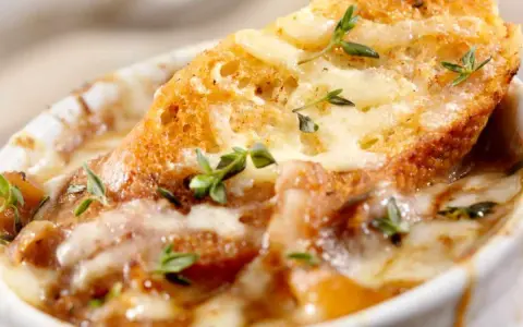 Una ricca zuppa di cipolle toscana, con crostini dorati e formaggio fuso, guarnita con timo fresco.