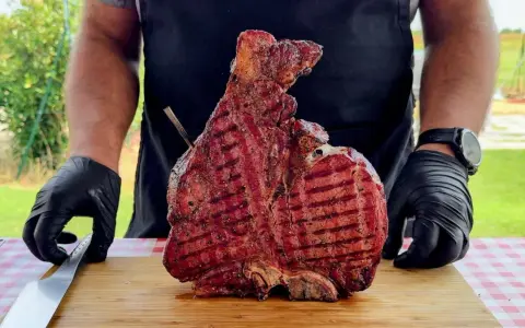 Un cuoco con guanti neri mostra una succulenta bistecca alla fiorentina appena grigliata, pronta per essere servita. Un esempio perfetto di come cucinare la bistecca alla fiorentina.