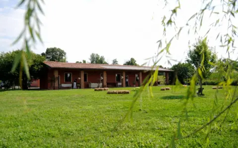Un'accogliente fattoria didattica alle Fornaci, con un edificio rosso, balle di fieno e un prato verde.