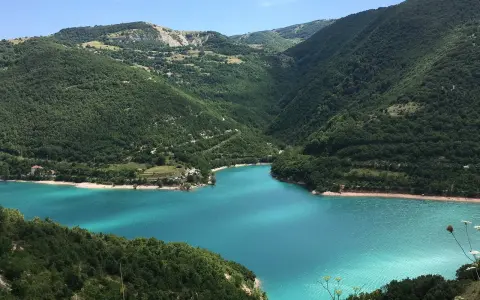 Un lago turchese incastonato tra colline verdi, ideale per il trekking nelle Marche.