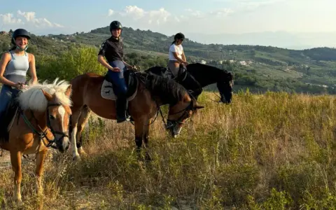 Tre ragazze in sella a cavalli godono di splendide passeggiate a cavallo in Abruzzo, tra colline verdi e cielo azzurro.