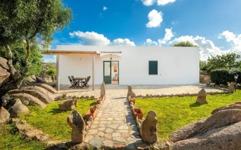 Un sentiero in pietra conduce a un bianco casolare, circondato da rocce granitiche e vegetazione mediterranea. Ideale per scoprire gli agriturismi Sardegna nord.