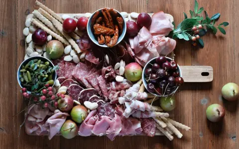 Tagliere con salumi tipici lombardi, frutta, sottaceti e grissini su un tavolo di legno.
