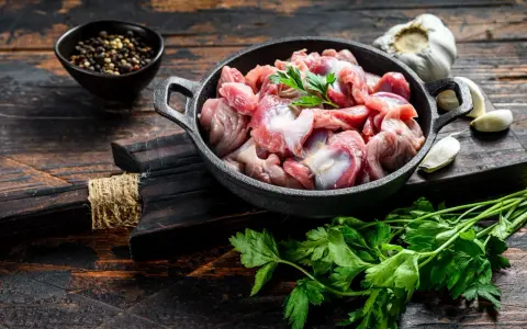 Piatto toscano con interiora di pollo crude in padella, con aglio, pepe e prezzemolo su tagliere di legno scuro.