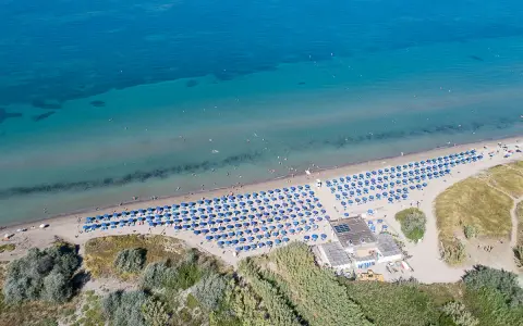 Spiaggia attrezzata con ombrelloni blu, ideale per campeggi in Toscana sul mare per bambini. Acqua cristallina e gente che si gode il sole.