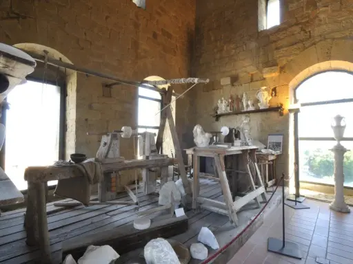 Laboratorio di scultura con attrezzi antichi e statue in marmo, che evoca la tradizione dell'alabastro toscana.
