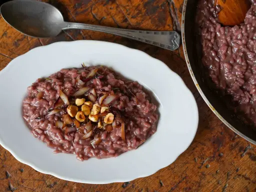 Risotto rosso con cipolla caramellata e nocciole, un classico tra i piatti tipici di Verona, servito su un piatto bianco con un cucchiaio d'argento.