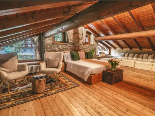Accogliente camera con camino, travi in legno a vista, letto comodo, poltrone soffici e un tappeto decorato.