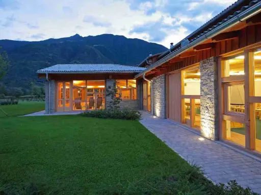 Edificio moderno con pietra e legno, circondato da prati verdi, con ampie vetrate che illuminano l'interno. Sembra un luogo ideale per fattorie con ristorante.