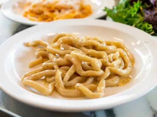 Pici cacio e pepe, un classico tra i piatti tipici di Siena, serviti su un piatto bianco.