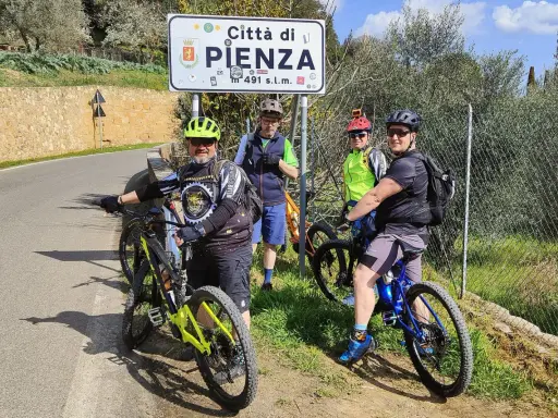 Quattro ciclisti si fermano per una foto con il cartello "Città di Pienza" durante un'avventura in bici nel Val d'Orcia.
