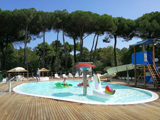 Bambini felici in piscina con gonfiabili, scivoli e giochi d'acqua. Perfetti campeggi Emilia Romagna per bambini, un'oasi di divertimento sotto i pini.