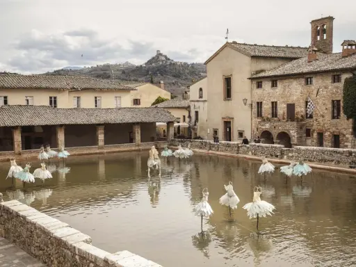 Bagno Vignoni: cosa vedere? La vasca termale con installazioni artistiche di abiti da ballo e un cavallo bianco.