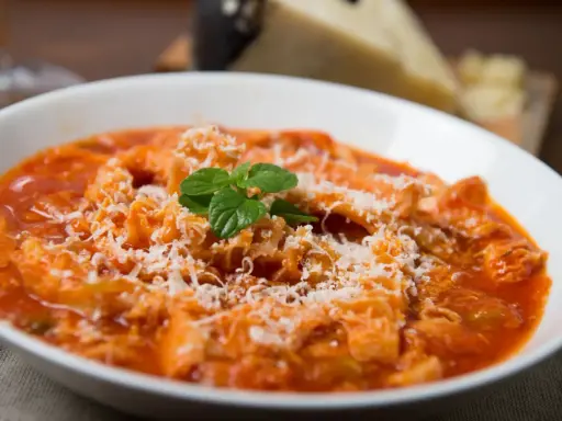 Trippa alla romana, uno dei piatti tipici del Lazio, servita in una ciotola bianca con parmigiano grattugiato e una fogliolina di menta.