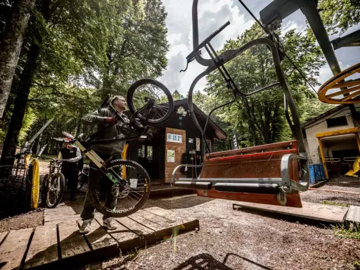 Ciclista porta la sua bici verso gli impianti di risalita ad Amiata, pronto per un'avventura in mountain bike.