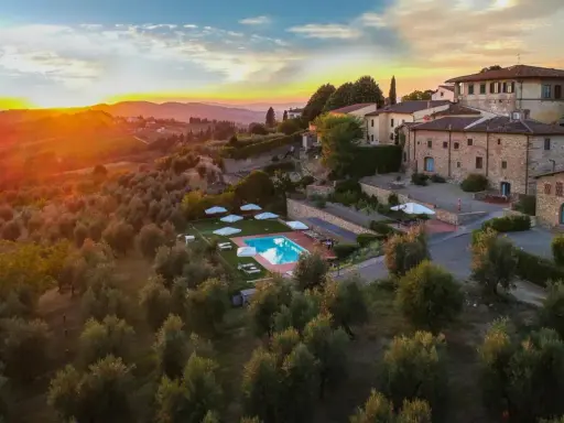 Un tramonto dorato illumina un agriturismo con piscina, immerso tra ulivi e colline, perfetto per un tour della Toscana.