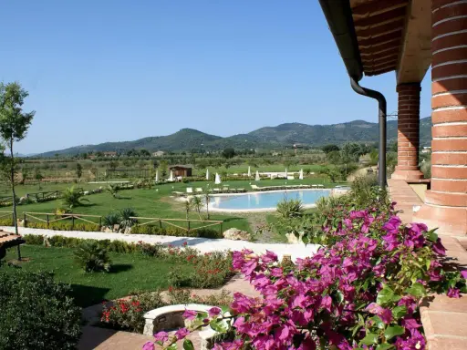 Un angolo di campagna toscana lungo il mare, con piscina, giardini curati e colline verdi all'orizzonte.