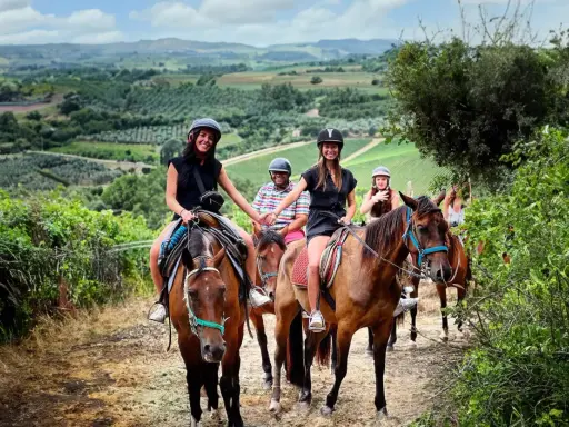 Un gruppo di amici si gode una **passeggiata a cavallo toscana** tra colline verdi e vigneti. Sorridono felici, immersi nella bellezza del paesaggio.