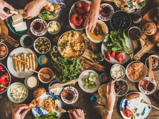 Un ricco banchetto per vacanze enogastronomiche: formaggio, olive, pane, miele, verdure fresche e piatti caldi, tutto condiviso in un'atmosfera conviviale.
