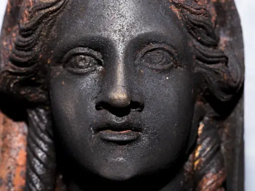 Volto di bronzo scuro, un dettaglio dei bronzi di San Casciano dei Bagni, con capelli a onde e trecce.