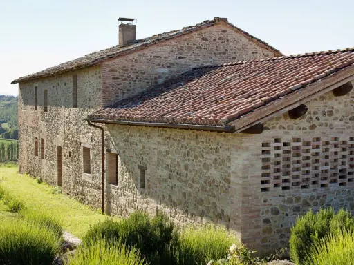 Un casale in pietra e mattoni, ideale per vacanze in Umbria montagna, immerso nel verde con tetto in coppi e un muro traforato.