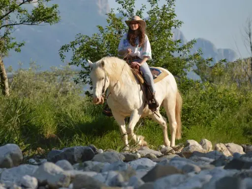 Giovane donna con cappello da cowboy e cavallo bianco durante una passeggiata a cavallo in Campania, tra rocce e vegetazione rigogliosa.