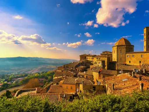 Un borgo toscano al tramonto, con tetti in cotto e un campanile svettante. Curiosità sulla Toscana: questo paesaggio evoca storie antiche.