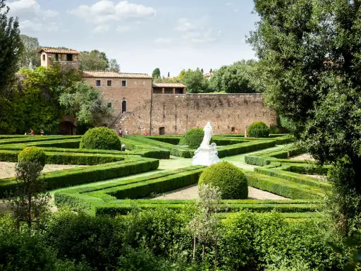 Giardino all'italiana con siepi geometriche, una statua bianca e un antico borgo toscano da visitare sullo sfondo.