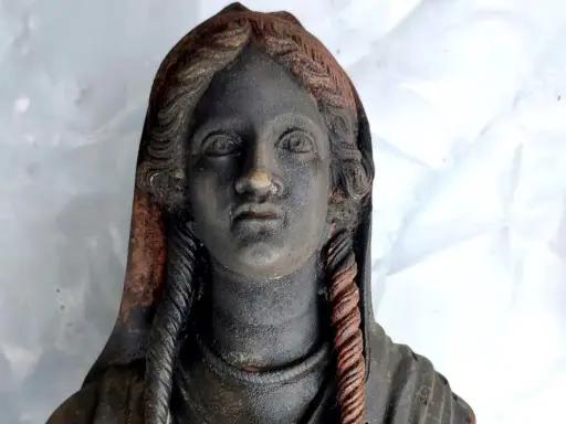 Statua antica ritrovata nel santuario di San Casciano dei Bagni, con capelli intrecciati e volto enigmatico.