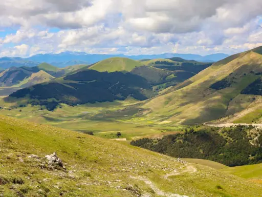 Panoramica dei Monti Sibillini, un paesaggio verdeggiante con dolci colline e valli, ideale per scoprire cosa vedere in questa zona.