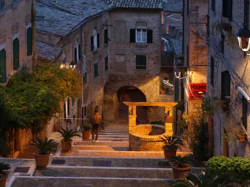 Un vicolo suggestivo a Montefeltro, cosa vedere: un pozzo antico, scalinate in pietra e luci soffuse creano un'atmosfera magica.