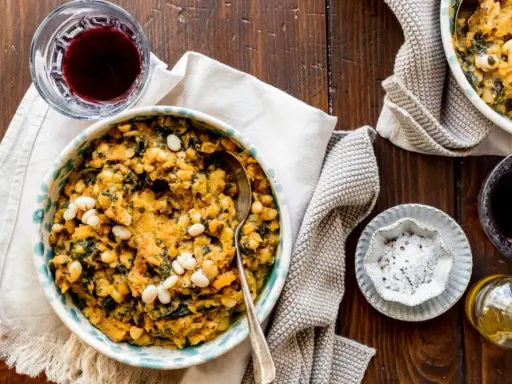 Un piatto fumante di fagioli e verdure, un classico delle ricette toscane, accompagnato da vino rosso e olio d'oliva.