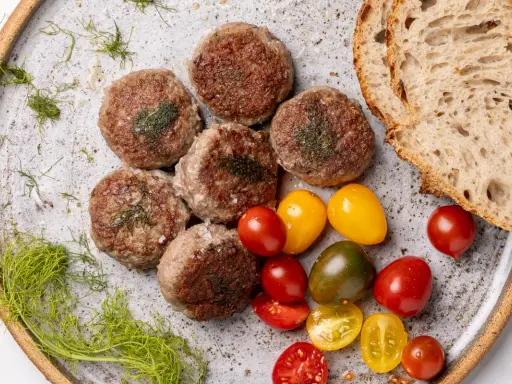 Polpette di cinta senese su piatto rustico, con pomodorini colorati, pane casereccio e finocchietto selvatico.