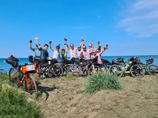 Un gruppo di ciclisti festeggia sulla spiaggia, pronti per un'avventura di cicloturismo in Toscana.