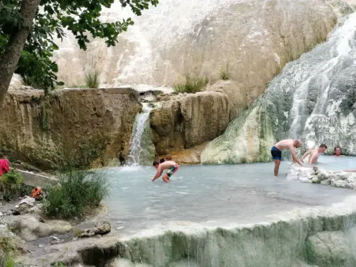 Persone si rilassano nelle piscine termali naturali di Castiglione d'Orcia, con cascate che scendono da rocce bianche.