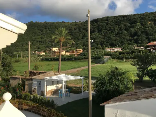 Un angolo di pace tra gli agriturismi in Calabria. Un pergolato bianco con tavolino e sedie blu, circondato da verde e colline rigogliose.
