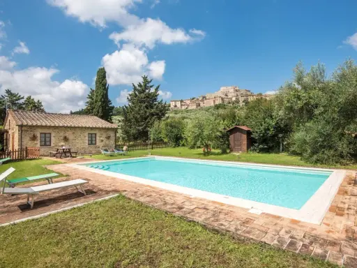 Piscina in un casale in pietra nel Val d'Orcia, Italia, con un borgo medievale sullo sfondo.