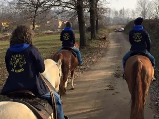 Cavalcata autunnale nei maneggi Piemonte, tre persone a cavallo su un sentiero sterrato tra alberi spogli e campi.