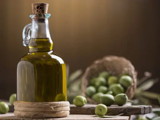 Bottiglia di olio extravergine di oliva, con olive verdi in cestino e su tagliere. La differenza tra olio di oliva e extravergine è la qualità.