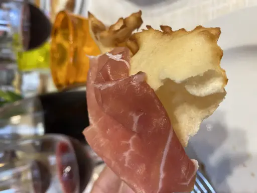 Fetta di gnocco fritto con prosciutto crudo, un classico dei piatti tipici Parma, accompagnato da vino rosso.
