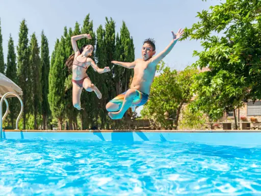 Bambini che saltano in piscina, una gioiosa Pasqua in Toscana tra cipressi e sole.