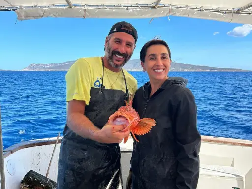 Coppia felice in barca, lui mostra un pesce rosso appena pescato, un'esperienza di pesca turismo indimenticabile.