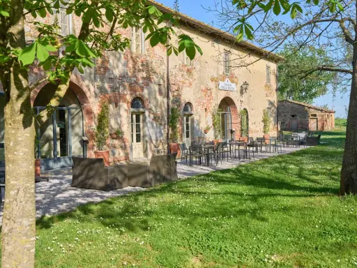 Antica locanda nel Val di Chiana, con tavoli all'aperto e un prato fiorito.