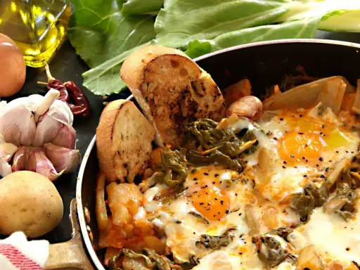 Uova cotte in padella con verdure, patate, aglio, peperoncino e pane tostato. Un piatto rustico e saporito, perfetto per una colazione o un pasto veloce.